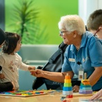 A woman hands a toy to a young child and her mother.