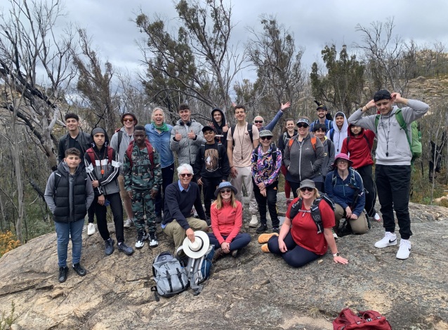Group of hikers sitting and standing together on a boulder with trees in the background