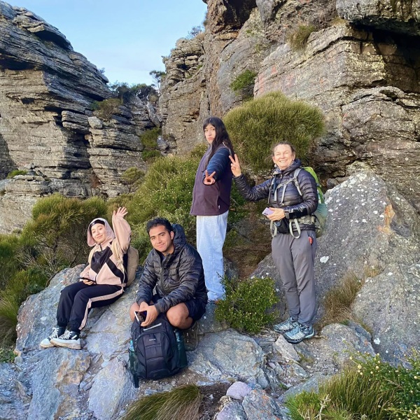 Group of people on a hike standing and sitting on front of a rock formation