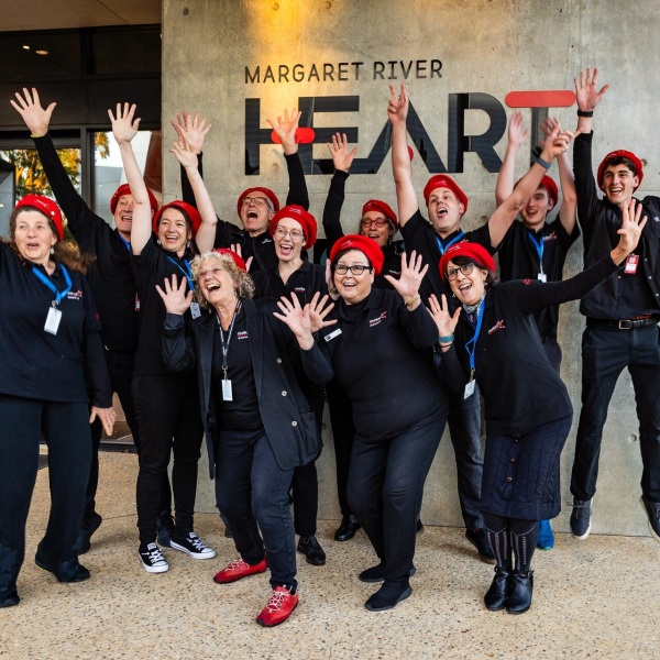 Members of margaret river heart in navy blue uniform with red hats smiling and posing with arms and fingers spread