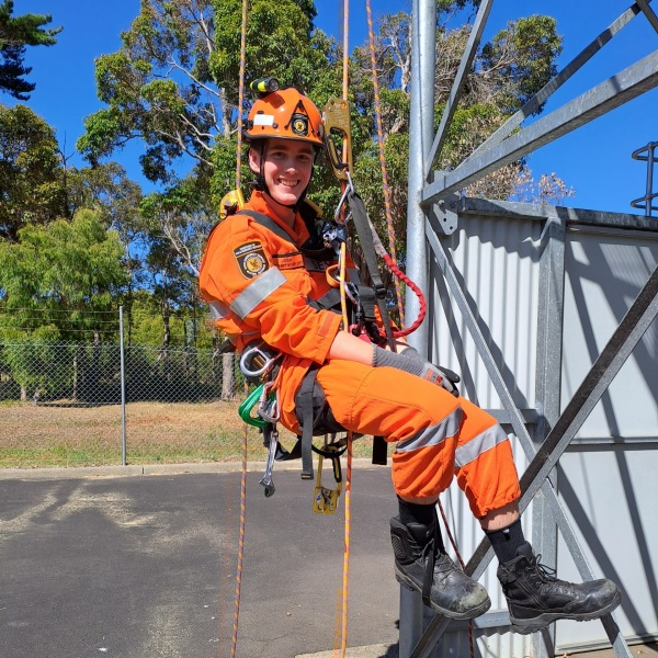 Man in orange high visibility uniform smiling whilst suspended from ropes
