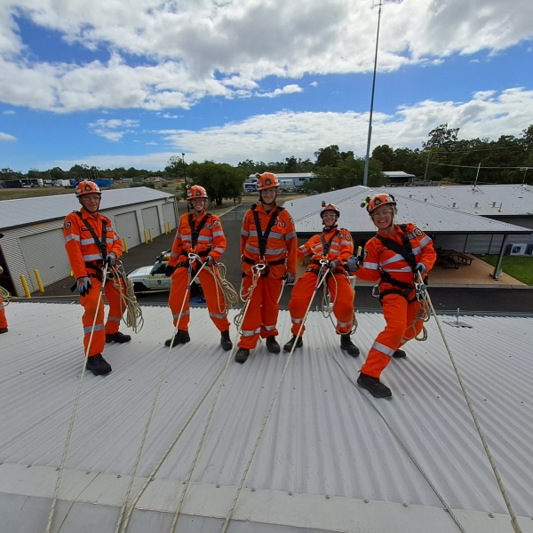 Group of people in orange high visibility uniforms fastened to the roof with ropes