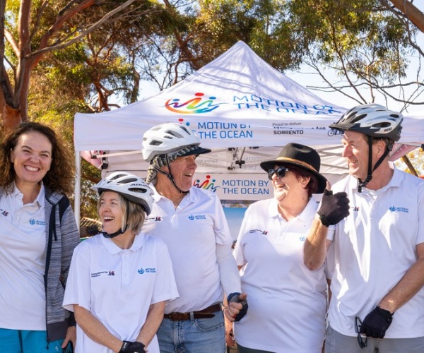 A group of people wearing white shirts and helmets and smiling at the motion by the ocean event