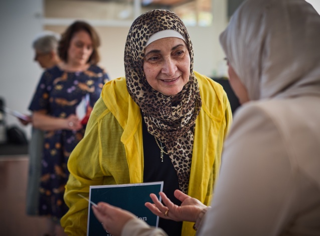 Woman in a leopard print headdress and yellow shawl speaking with another woman in a headdress