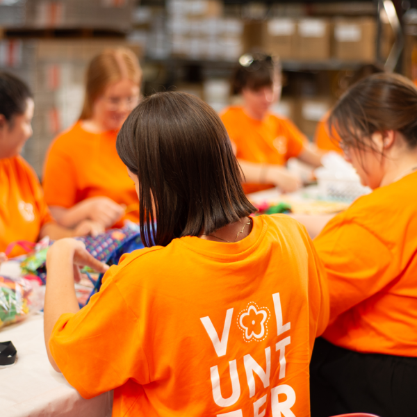 Girls in orange volunteering shirts sitting at a table and working on some crafts