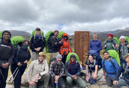 A group of people with hiking gear together near the sign for the Overland track on an overcast day