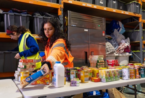 A volunteer lays a box of pasta on a table of sorted food donations