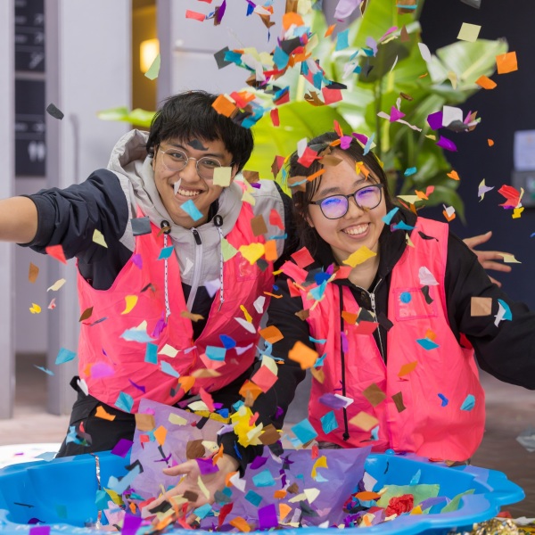 Two young volunteers in vests throwing confetti into the air